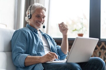 Smiling man in headset watch webinar or training on modern computer, male call center agent or telemarketer work consult client online