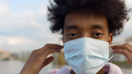 Close up portrait of cheerful afro guy putting on and off safety mask standing outdoors
