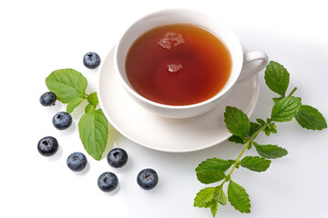 A Cup of black tea on a saucer with mint leaves and blueberries on a white isolated background.