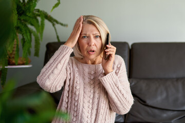 Sad senior woman in a phone call sitting on a sofa in the living room