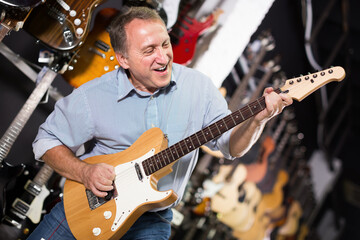 Obraz premium Happy male is playing on wooden electric guitar in music studio
