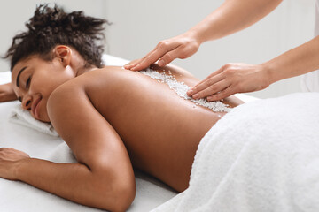 Joyful black lady getting healing salt massage at modern spa