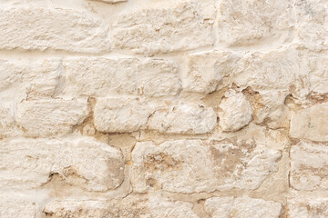 Old fashioned surface of historical building wall made of weathered brown bricks covered with white flaked stucco at bright sunlight extreme close view