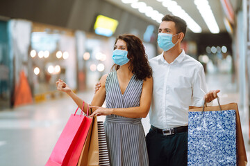 Young couple holding shopping bags, looking upon showcase and discuss shopping inside of mall. Shopping in the coronavirus epidemic. Sale, consumerism, Black friday concept. 