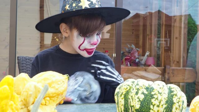 boy wearing scary jocker or clown makeup and halloween costume play with scull outdoor, selective focus, 4K
