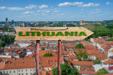 Wooden arrow road sign with word Lithuania against Vilnius old town background. Travel to Lithuania concept.