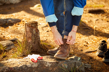 unrecognizable cropped man is tying laces on shoes for hiking, stand on rocks preparing fore climbing mountains