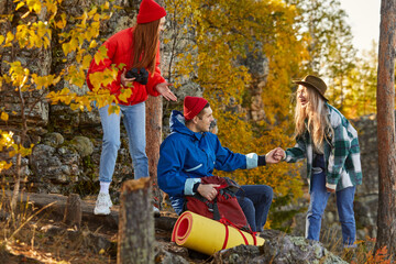 friends help each other to climb mountains, happy tourists spend free time in the forest, laugh