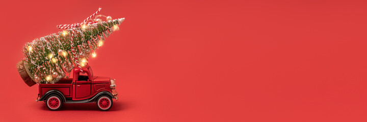 Banner photo of red small retro toy truck with sparkling Christmas tree lights on truck body on red background. Delivery, christmas, New Year concept. Copy space, selective focus.