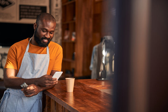 Cheerful Afro American man using cellphone in barbershop