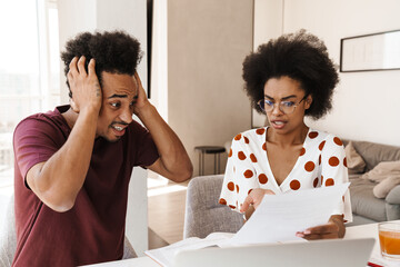 Portrait of worried couple paying bills online via laptop