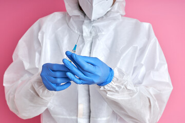 Fototapeta premium biological hazard, covid-19 concept. close-up male nurse, scientist in a protective suit and mask holding an injection syringe and vaccine. vaccine from, flu, coronavirus, ebola