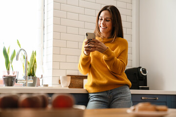 Beautiful caucasian woman smiling and using cellphone in apartment - Powered by Adobe