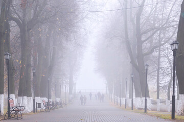 Alley of the city park in the autumn in the fog. Vague silhouettes of people going nowhere. Mist, haze, low visibility.