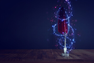 Old feather quill ink pen with inkwell over wooden desk infront of black wall background. Vintage old style and filtered. Conceptual photo on history, education, fantasy and literature topic