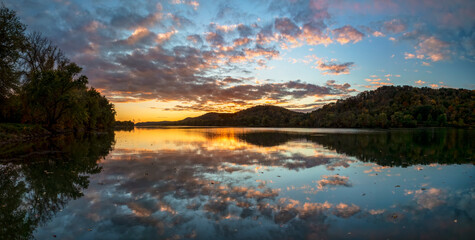 Dramatic clouds in a colorful sunset sky are reflected on the beautiful Ohio River, as photographed from Paden City, West Virginia, with the hills along the valley displaying beautiful autumn leaves.