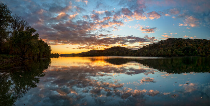 Dramatic clouds in a colorful sunset sky are reflected on the beautiful Ohio River, as photographed from Paden City, West Virginia, with the hills along the valley displaying beautiful autumn leaves.