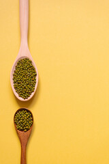 Two wooden spoons with mung bean on a yellow background.