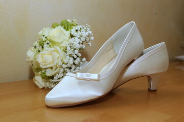 white wedding shoes with a small white bow  for woman with white wedding bouquet with roses in the background 