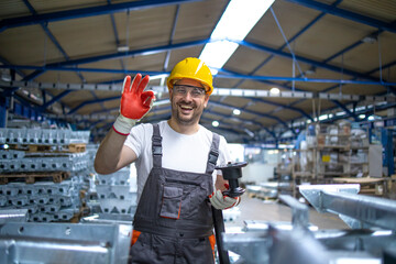 Portrait of factory worker in protective equipment holding thumbs up in production hall.