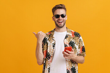 Cheerful handsome guy pointing finger aside and using mobile phone