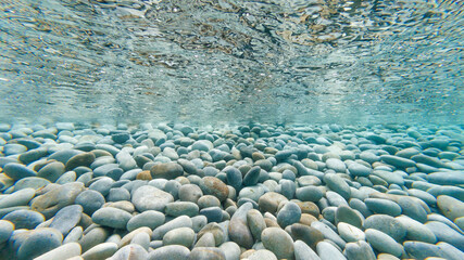Underwater photo of pebbles on tropical beach reflecting on the underside of the surface of the...