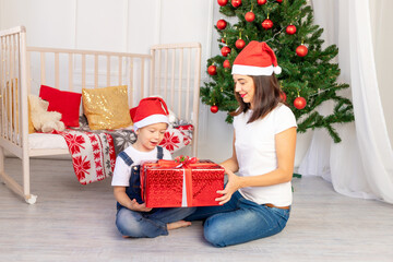 Obraz na płótnie Canvas mom gives a child a gift in a large red box for new year or Christmas in the children's room with a new year's interior near the Christmas tree