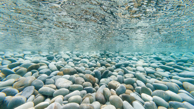 Underwater photo of pebbles on tropical beach reflecting on the underside of the surface of the ocean