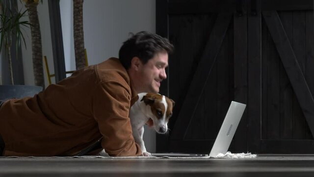 Man with a dog is working with laptop at home on a floor