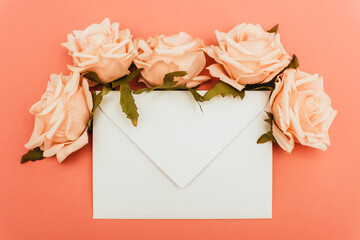 top view of white envelope and roses on coral background