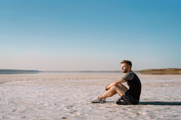 Fototapeta na wymiar Attractive young sportsman sitting at the salt lake