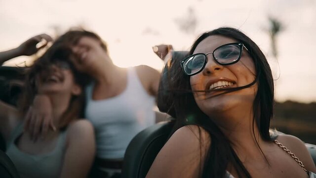 Slow motion shot of young women having fun in cabriolet at sunset