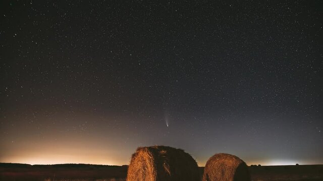 Comet Neowise C/2020 F3 In Night Starry Sky Above Haystacks In Summer Agricultural Field. Night Stars Above Rural Landscape With Hay Bales After Harvest. Agricultural Concept. 4K Timelapse