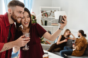 Image of joyful friends taking selfie on cellphone while drinking wine
