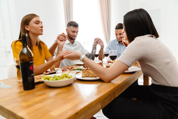 Image of happy multinational friends praying before lunch with holding hands together