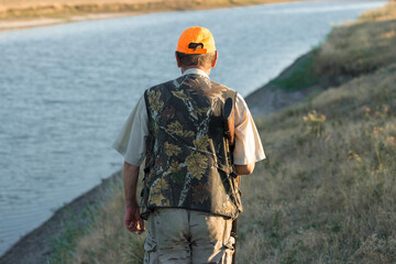 Duck hunter with shotgun walking through a meadow. .Rear view of a man with a weapon in his hands.