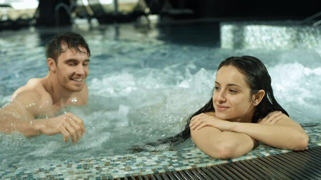 Beautiful couple meeting in spa pool. Guy and girl relaxing in whirlpool inside