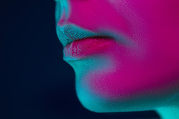 Lips. Close up portrait of female fashion model in neon light on dark studio background. Beautiful caucasian woman with trendy make-up and well-kept skin. Vivid style, beauty concept. Copyspace