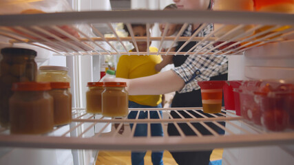 Caucasian mother with mixed race baby kid and toddler son opening fridge and taking bottle of milk