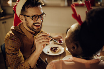 Cheerful man feeding his girlfriend during Christmas dinner at home.