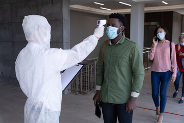Health worker wearing protective clothes checking temperature of businessman
