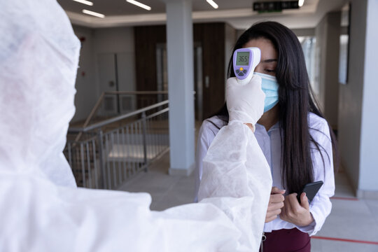 Health worker wearing protective clothes checking temperature of businesswoman