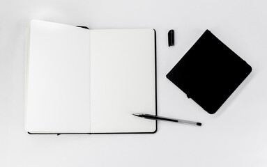 Black small closed square notepad and large open notebook with blank white pages and gel pen with cap
