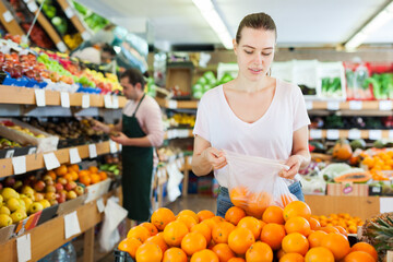Young woman customer choosing fresh oranges on the supermarket
