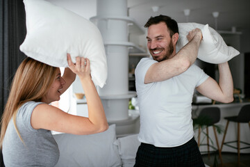 Fototapeta premium Husband and wife fighting pillows on the bed. Young couple having fun at home.