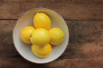 Ripe yellow lemons in a bowl on wooden table. Flat lay, copy space. Rustic style composition