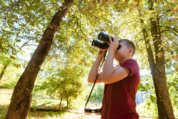 A teenage boy on a hike looks through binoculars on the road in
