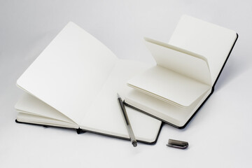 Black gel pen lie in unfold large notebook  and open small notepad with blank white pages. Light background.