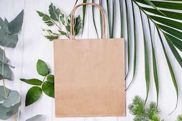 Craft paper shopping bag mockup on the table with green leaves