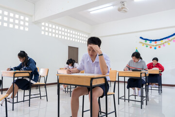 Fototapeta na wymiar Students Asian undergraduate testing of examination in room sitting serious on row chair doing final exams in classroom with Thailand uniform